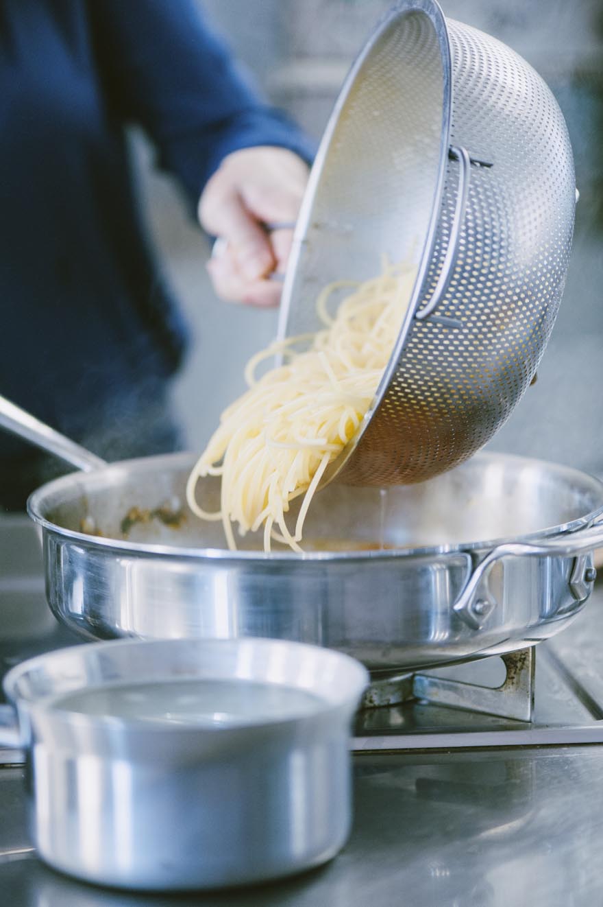Spaghetti scolati dal colino e versati nella padella con il sugo