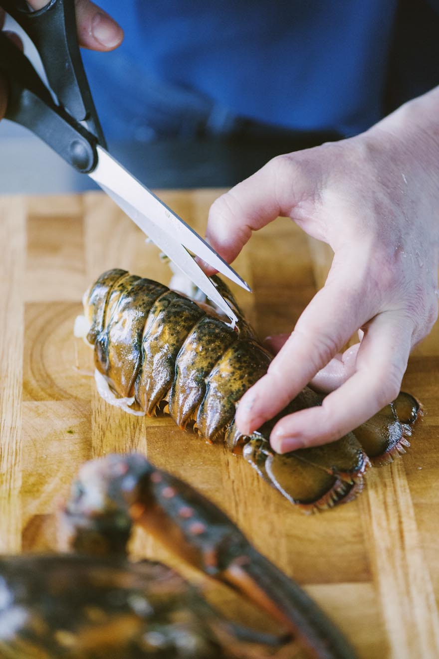 Mani che incidono il carapace di un astice crudo con le forbici sul tagliere
