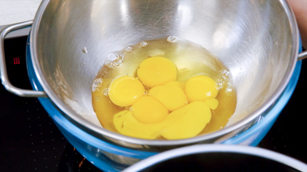 Uova intere e tuorli sgusciati in una ciotola di acciaio a bagnomaria, pronti per la crema della carbonara