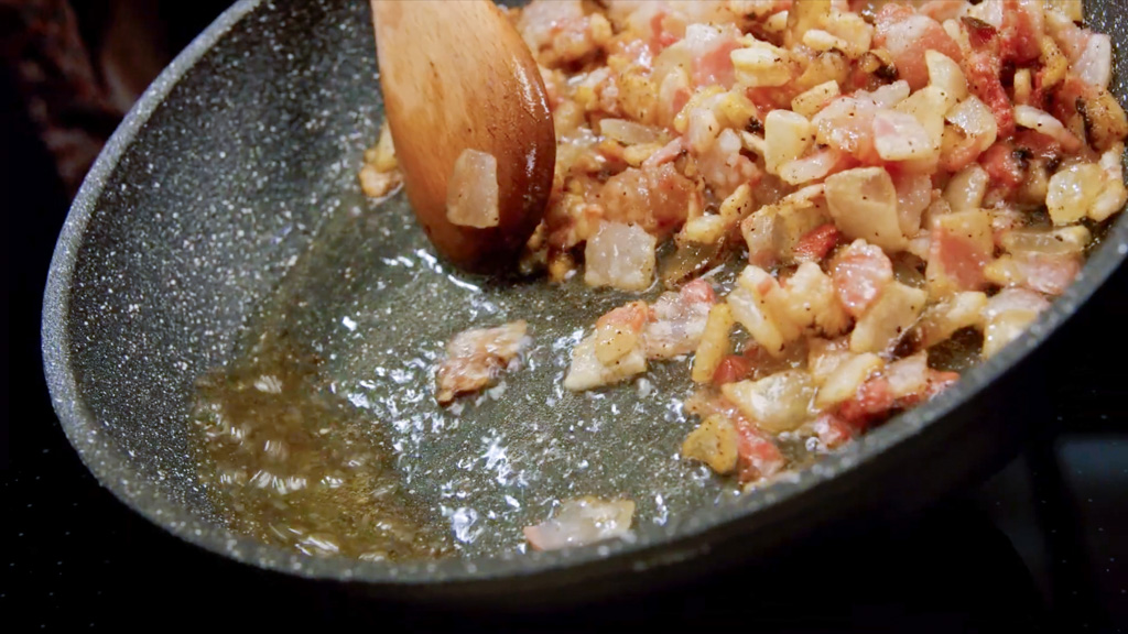 Guanciale a cubetti che rosola con cipolla tritata, mescolato con un cucchiaio di legno