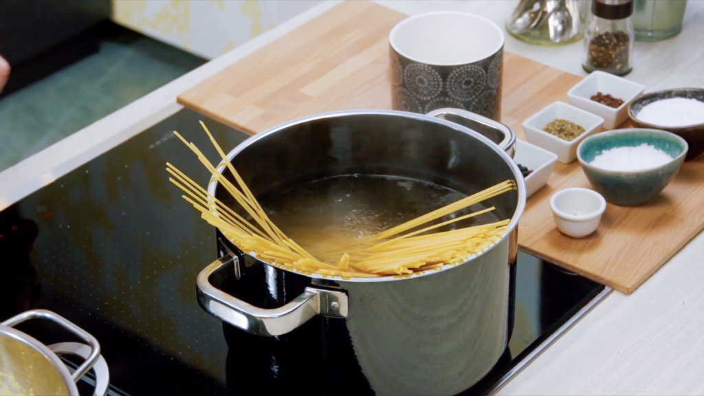 Spaghetti secchi immersi nell'acqua bollente in una pentola capiente sul fuoco
