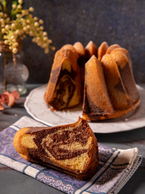 Ciambella marmorizzata con una fetta tagliata che mostra la spirale di cacao e impasto chiaro