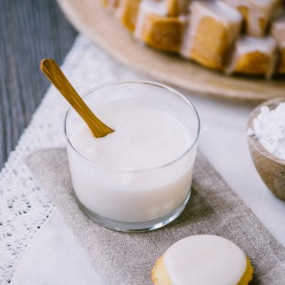 Glassa all'acqua in un bicchiere con cucchiaio di legno accanto a biscotti glassati