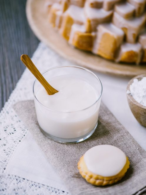 Glassa all'acqua in un bicchiere con cucchiaio di legno accanto a biscotti glassati