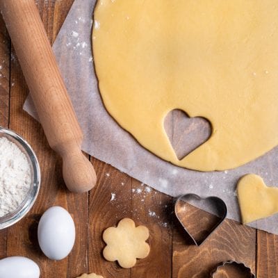 Pasta frolla stesa con biscotti ritagliati a cuore, fiore e cerchio pronti da infornare