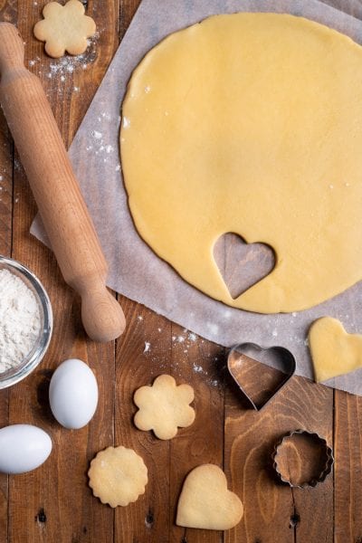 Pasta frolla stesa con biscotti ritagliati a cuore, fiore e cerchio pronti da infornare