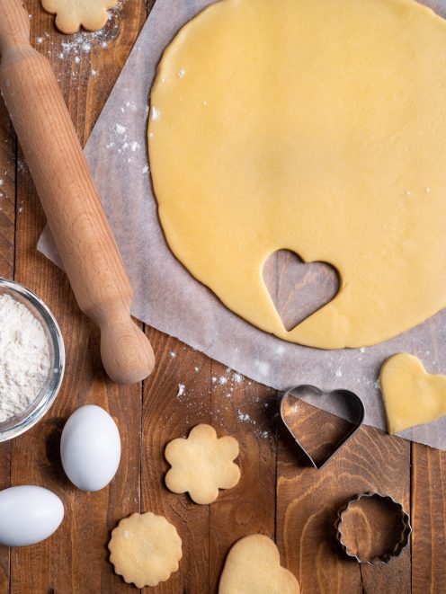 Pasta frolla stesa con biscotti ritagliati a cuore, fiore e cerchio pronti da infornare
