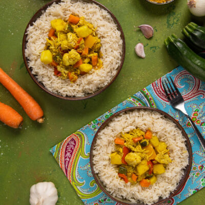 Pollo al curry con verdure servito su riso basmati, con carote, zucchine e patate al curry