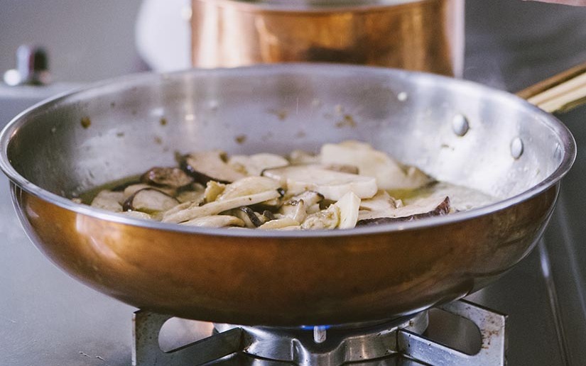 Funghi porcini a fette che rosolano in padella di rame sul fuoco vivo