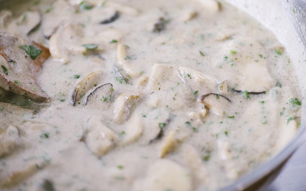 Funghi porcini a fette in una cremina densa con prezzemolo tritato, in cottura