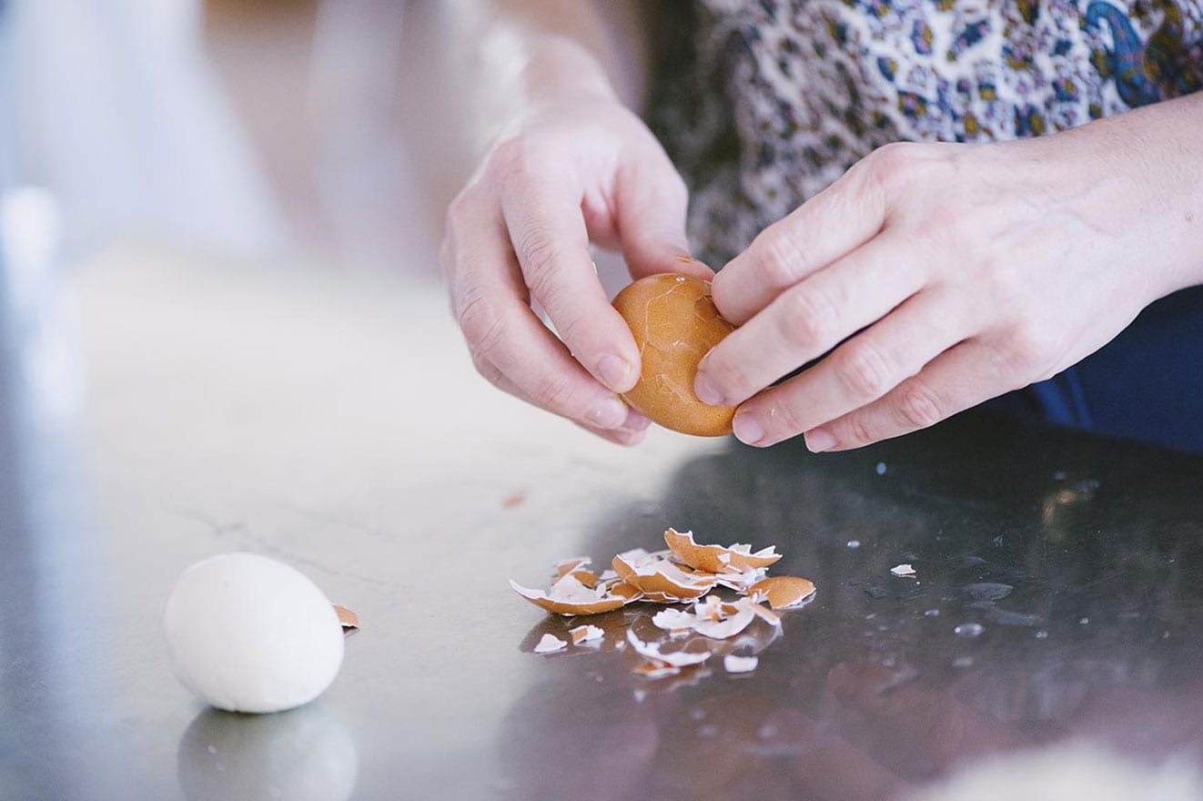 Mani che sgusciano un uovo sodo con frammenti di guscio sul piano di lavoro