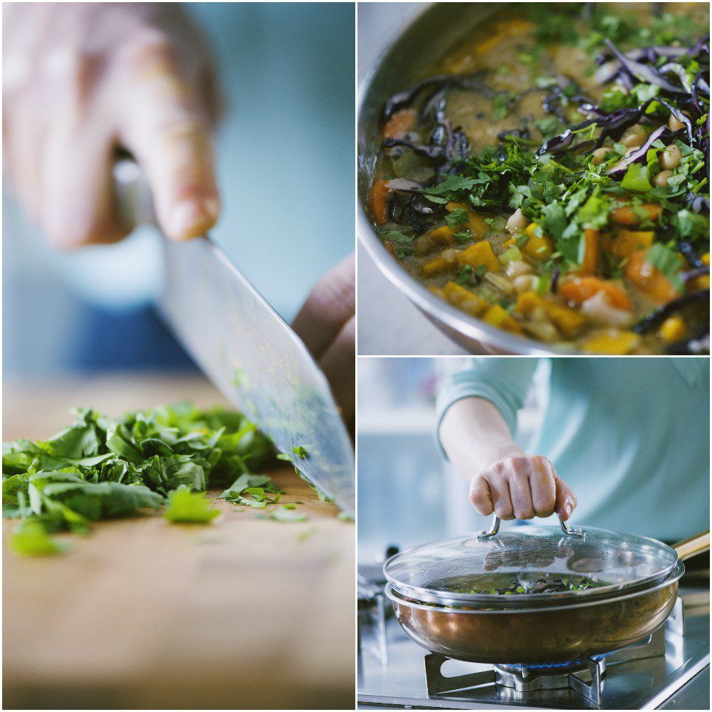 Coriandolo tritato sul tagliere, curry di verdure con ceci in cottura e padella coperta sul fuoco