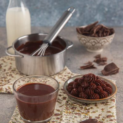 Ganache al cioccolato fondente liquida in un bicchiere e montata a ciuffi, con scaglie di cioccolato
