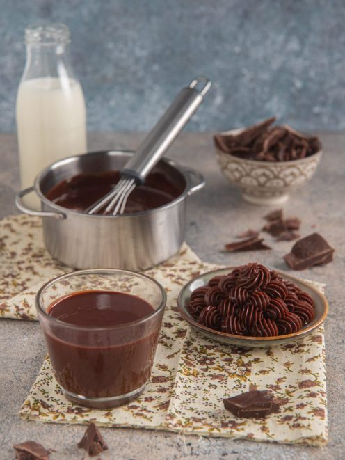 Ganache al cioccolato fondente liquida in un bicchiere e montata a ciuffi, con scaglie di cioccolato