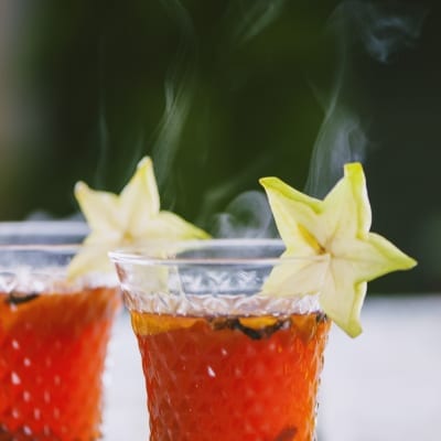 Punch di Natale caldo con liquido ambrato e rosso, guarnito con una fetta di carambola sul bordo del bicchiere