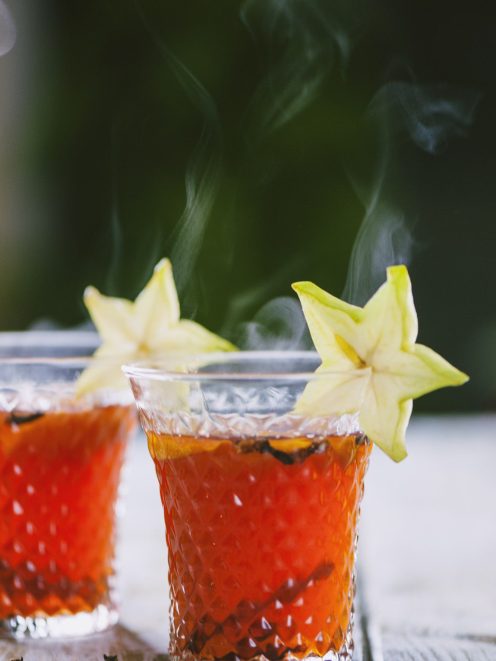 Punch di Natale caldo con liquido ambrato e rosso, guarnito con una fetta di carambola sul bordo del bicchiere
