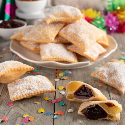 Bugie ripiene senza glutine fritte e spolverate di zucchero a velo, alcune aperte con marmellata