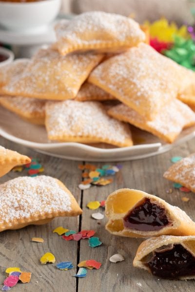 Bugie ripiene senza glutine fritte e spolverate di zucchero a velo, alcune aperte con marmellata