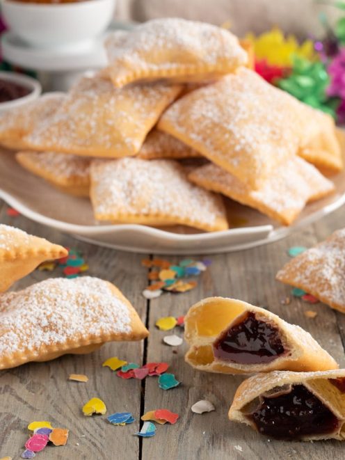 Bugie ripiene senza glutine fritte e spolverate di zucchero a velo, alcune aperte con marmellata