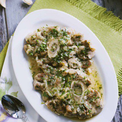 Ossobuco alla milanese con gremolata di prezzemolo, aglio e limone su vassoio da portata