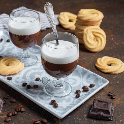 Bicerin servito in bicchiere con strati di cioccolato e panna montata, accompagnato da biscotti