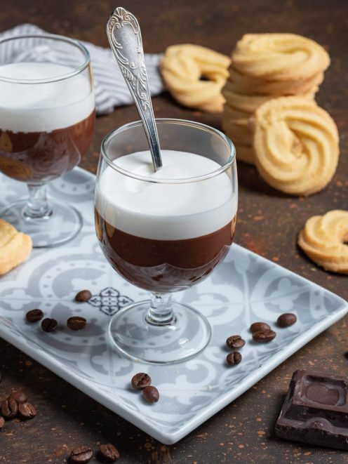 Bicerin servito in bicchiere con strati di cioccolato e panna montata, accompagnato da biscotti