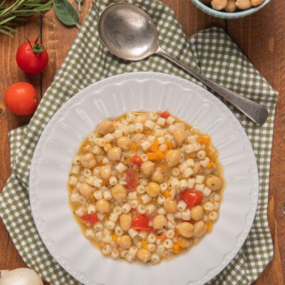 Pasta e ceci con ditalini, pomodorini e brodo saporito servita in un piatto fondo