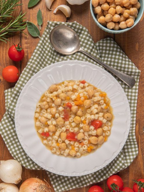 Pasta e ceci con ditalini, pomodorini e brodo saporito servita in un piatto fondo