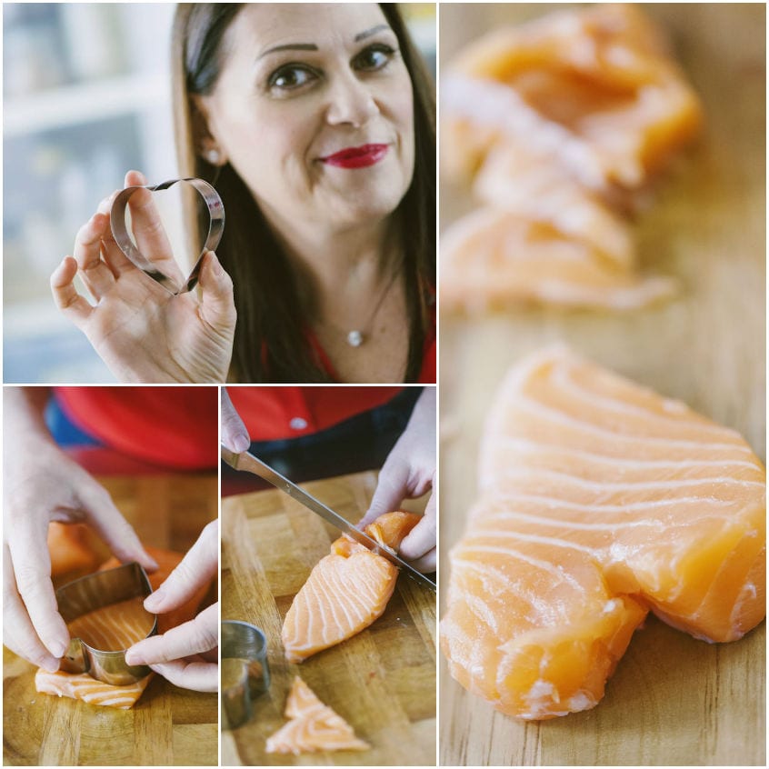 Mani che ritagliano cuori di salmone crudo con un coppapasta a forma di cuore su tagliere