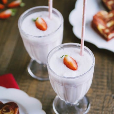 Milkshake alla fragola servito in due bicchieri con cannuccia e una fragola fresca in superficie