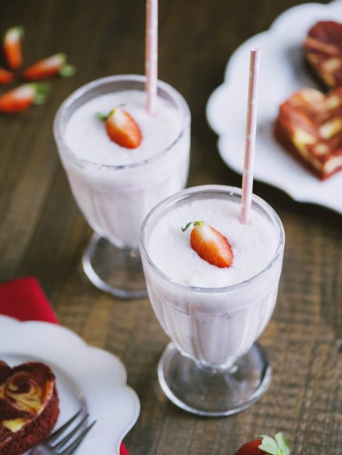 Milkshake alla fragola servito in due bicchieri con cannuccia e una fragola fresca in superficie