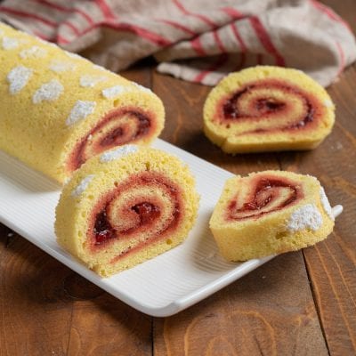 Rotolo alla confettura di fragole affettato, con la spirale di marmellata ben visibile e zucchero a velo