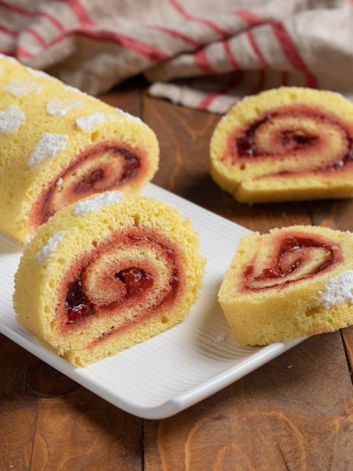 Rotolo alla confettura di fragole affettato, con la spirale di marmellata ben visibile e zucchero a velo