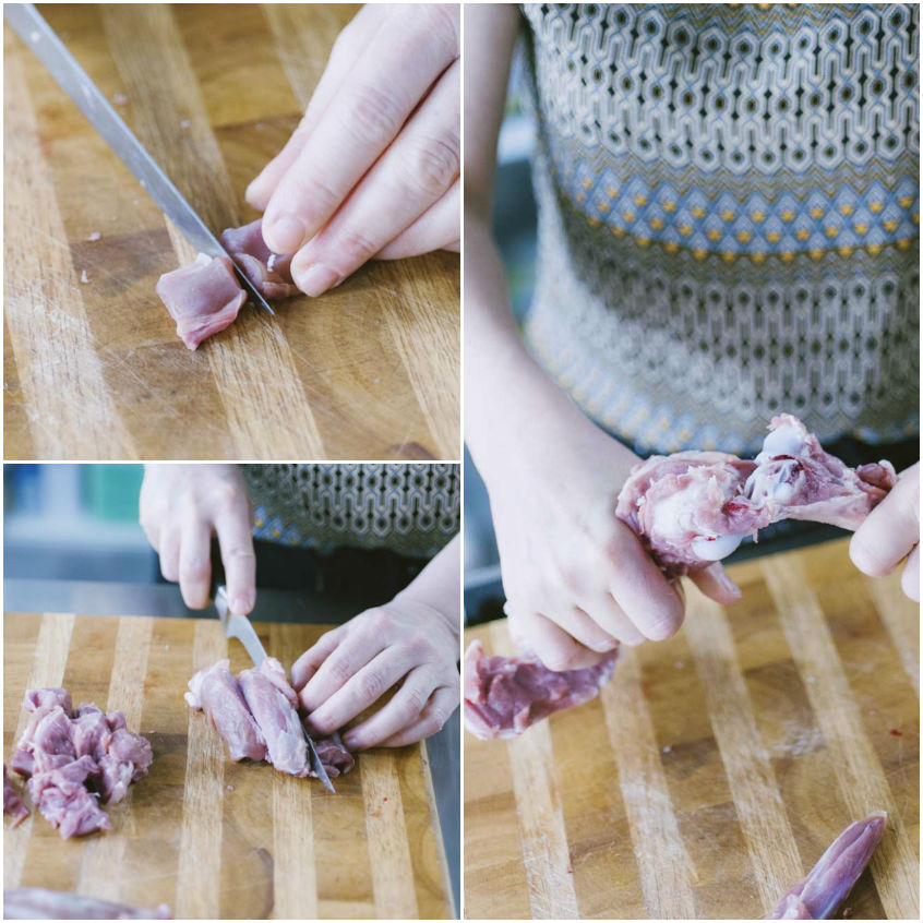 Mani che tagliano carne cruda a pezzi su un tagliere di legno