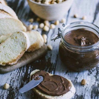 Crema spalmabile alle nocciole nel vasetto e spalmata su fetta di pane con nocciole intere