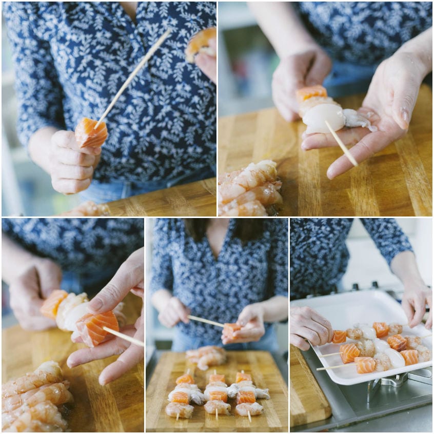 Mani che infilzano su stecchi di legno pezzi di salmone, gamberi e seppiolina per formare spiedini di pesce