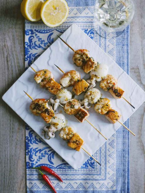 Spiedini di pesce con gamberi, calamari e salmone grigliati, conditi con erbe aromatiche