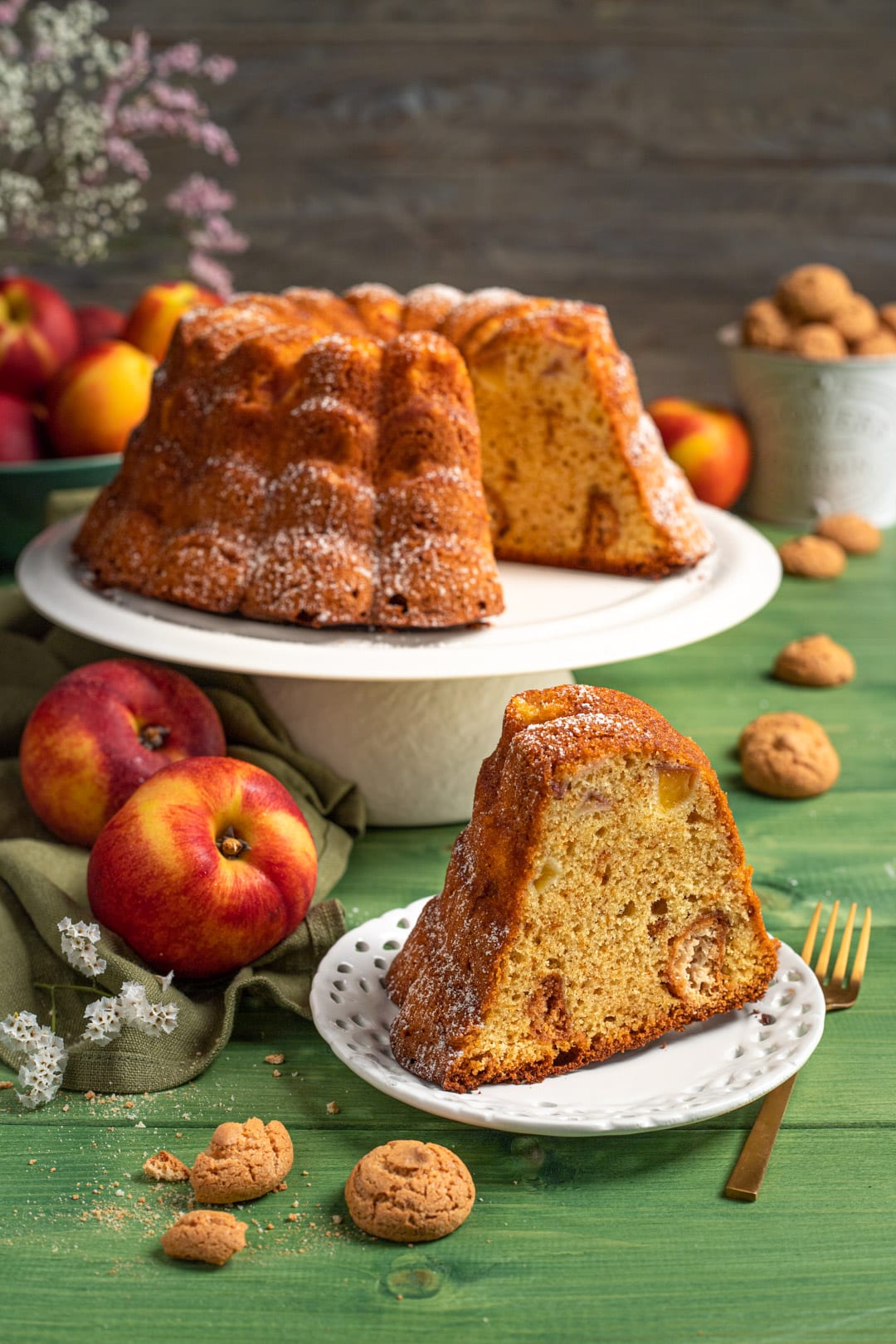 Ciambella con pesche e amaretti affettata, con zucchero a velo e la mollica che mostra i pezzi di frutta