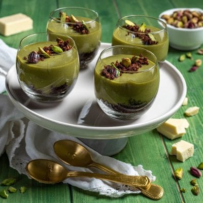 Cremoso al pistacchio e cioccolato bianco in bicchieri con base di sbriciolato al cacao e granella di pistacchi