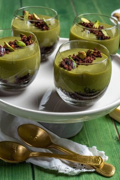 Cremoso al pistacchio e cioccolato bianco in bicchieri con base di sbriciolato al cacao e granella di pistacchi