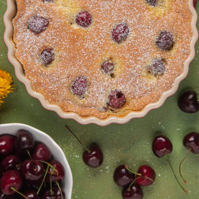 Clafoutis di ciliegie appena sfornato, con ciliegie intere affioranti e zucchero a velo in superficie