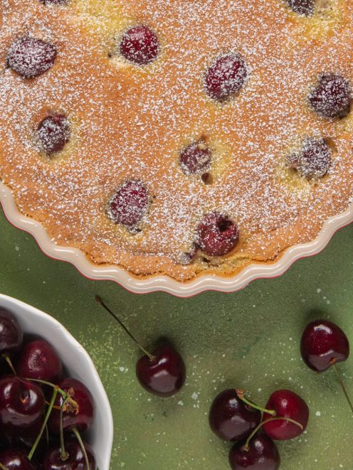 Clafoutis di ciliegie appena sfornato, con ciliegie intere affioranti e zucchero a velo in superficie