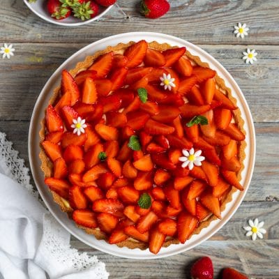 Crostata alle fragole con fette lucide di frutta fresca, crema e decorazioni di menta