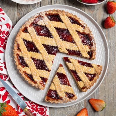 Crostata senza glutine con confettura di fragole, reticolo di pasta frolla e zucchero a velo, una fetta tagliata