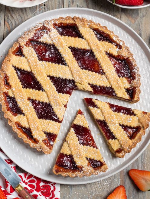 Crostata senza glutine con confettura di fragole, reticolo di pasta frolla e zucchero a velo, una fetta tagliata
