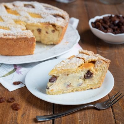 Crostata di ricotta alla romana con una fetta tagliata che rivela il ripieno cremoso con uvetta, spolverata di zucchero a velo