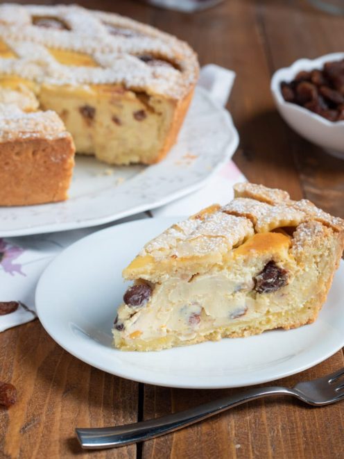 Crostata di ricotta alla romana con una fetta tagliata che rivela il ripieno cremoso con uvetta, spolverata di zucchero a velo