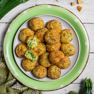 Polpette di zucchine dorate servite in abbondanza, una spezzata mostra il ripieno verde