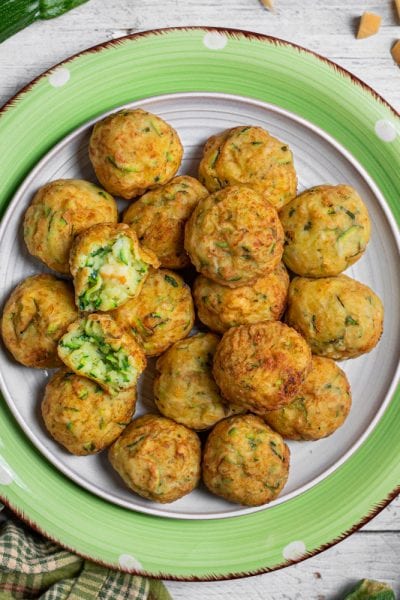 Polpette di zucchine dorate servite in abbondanza, una spezzata mostra il ripieno verde