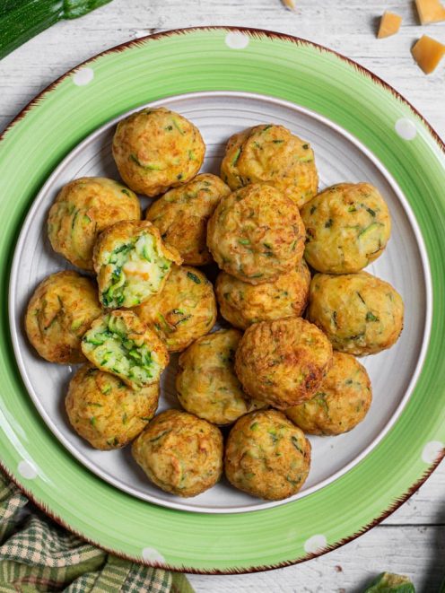 Polpette di zucchine dorate servite in abbondanza, una spezzata mostra il ripieno verde